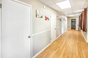 Hallway with gray walls, three white doors, wooden floors, and framed pictures hanging on the wall.