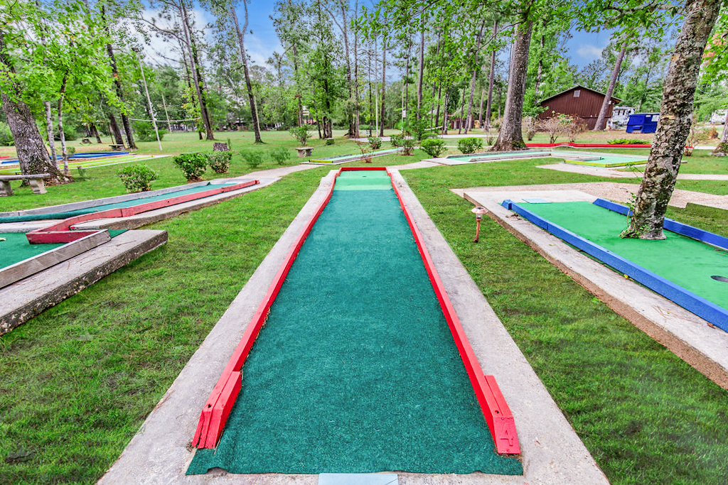 Outdoor mini-golf course with multiple colorful putting lanes surrounded by trees and benches in a wooded park setting