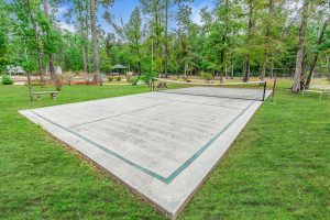 Outdoor concrete pickleball court with green boundary lines, surrounded by tall trees and natural scenery.