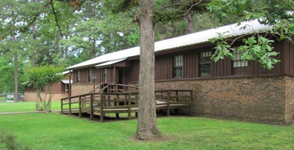 Bundick Lake RV Park Bundick Lake Retreat & RV Park in DeRidder, LA: brown brick and wood building, metal roof, trees, ramp entry, wheelchair accessible.