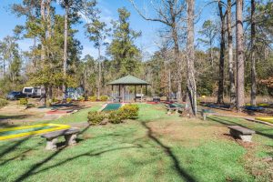 Bundick Lake RV Park Mini-golf course with gazebo, putting greens, and benches at Bundick Lake Retreat and RV Park in DeRidder LA, trees under blue sky.