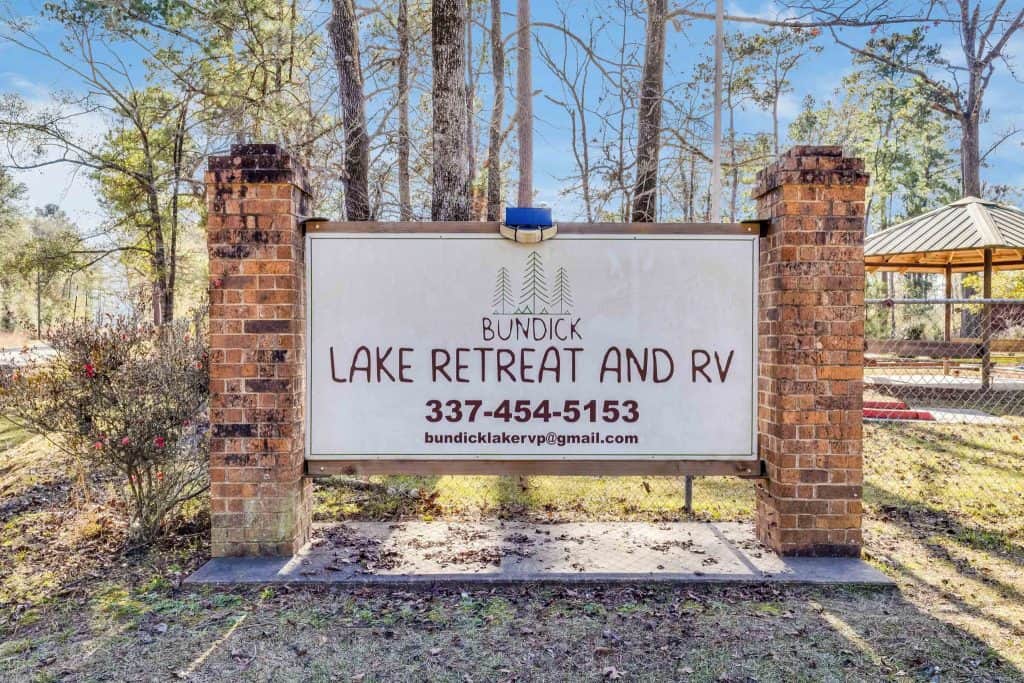 Bundick Lake RV Park Bundick Lake Retreat and RV Park sign in DeRidder Louisiana between brick columns, with contact info, trees, and pavilion visible.